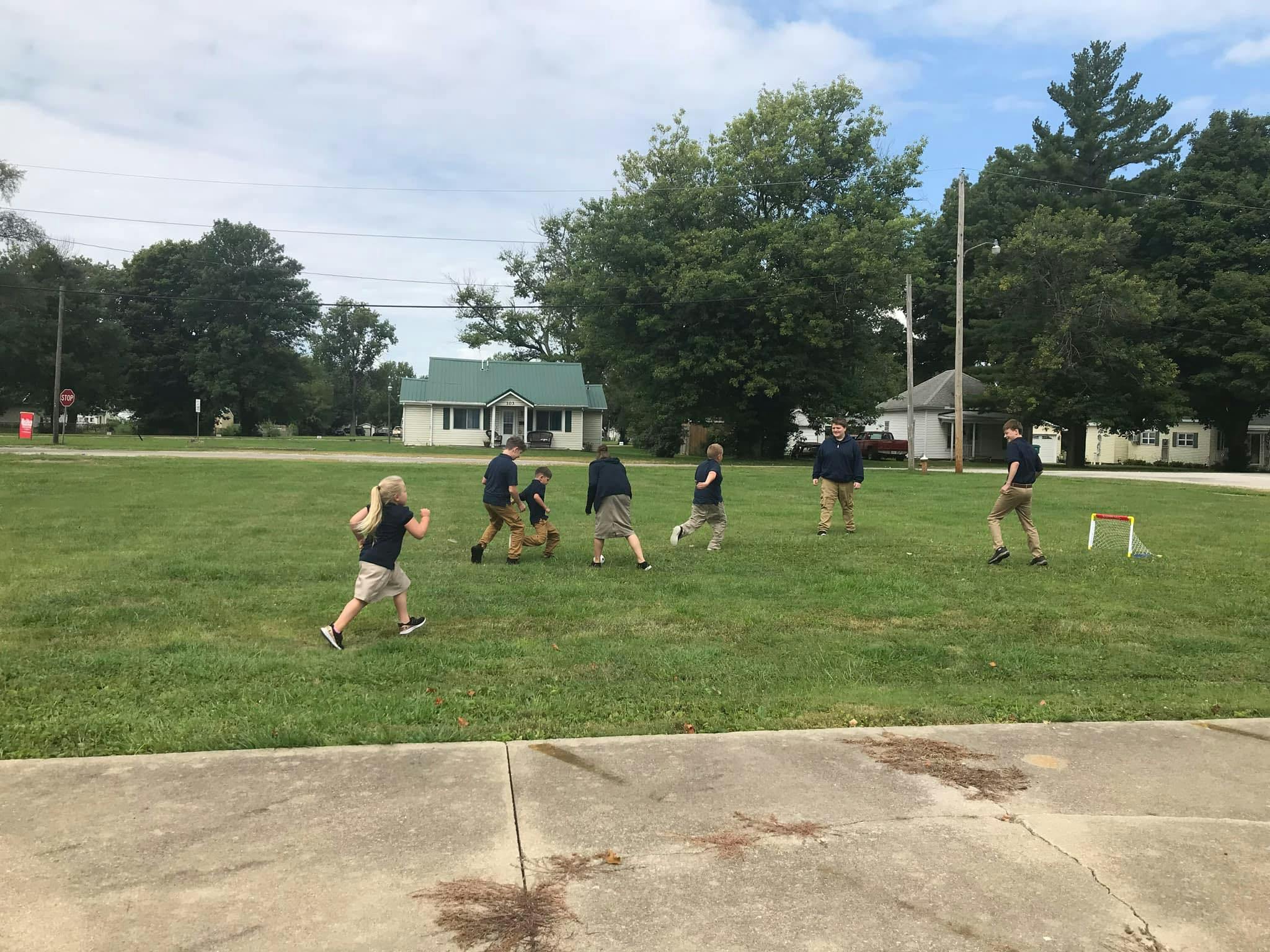 Group of children playing soccer on a grassy field near houses