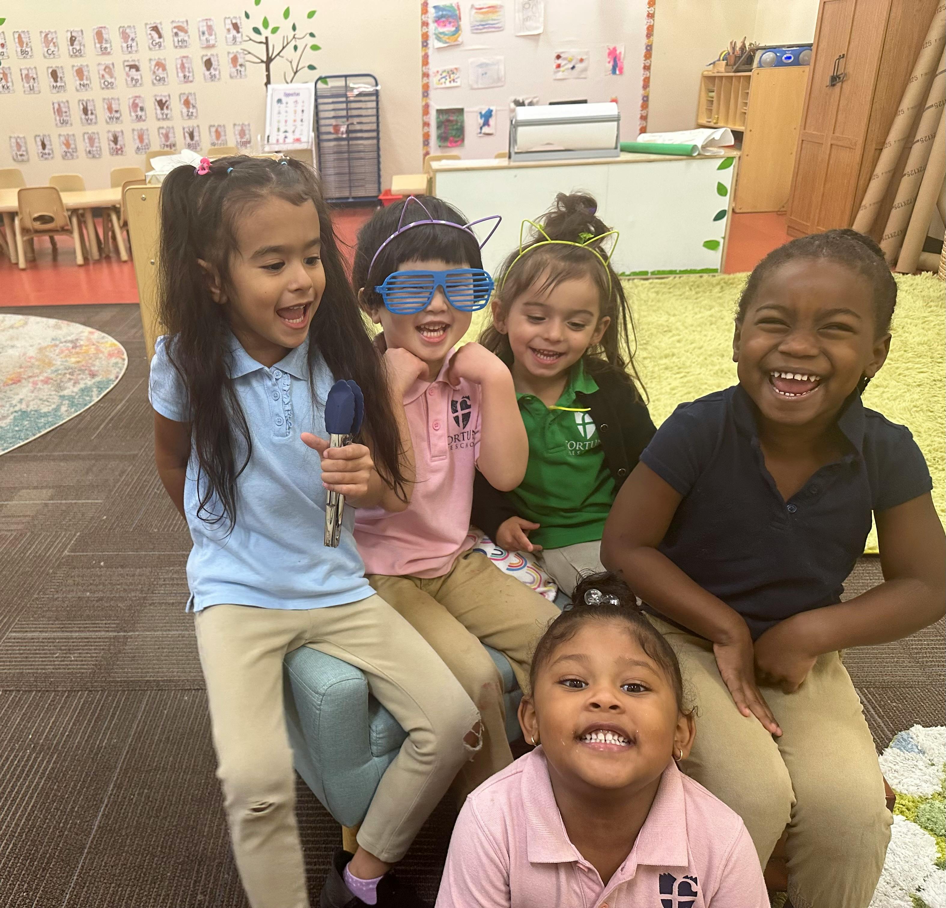 Five children in a classroom, one holding a toy microphone