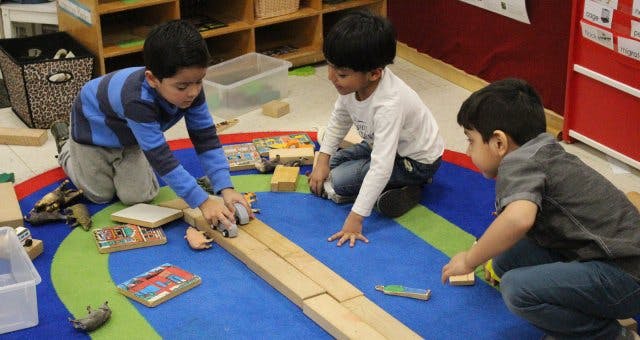 Three children playing with wooden blocks on a colorful rug