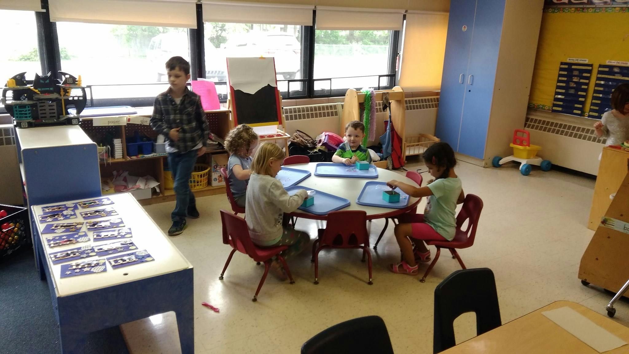 Person standing near children seated at a table in a classroom