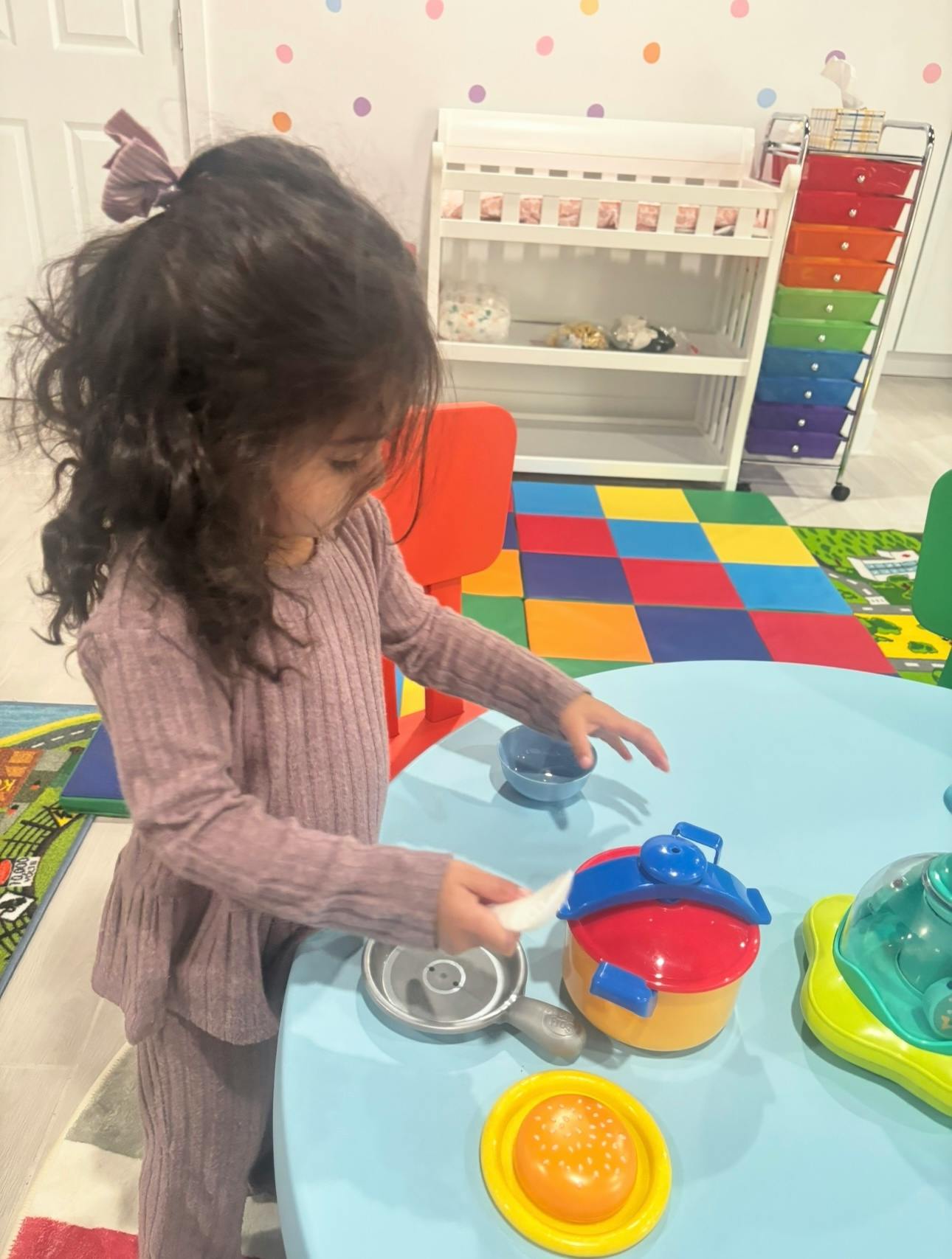 Child playing with toy kitchen set at a blue table
