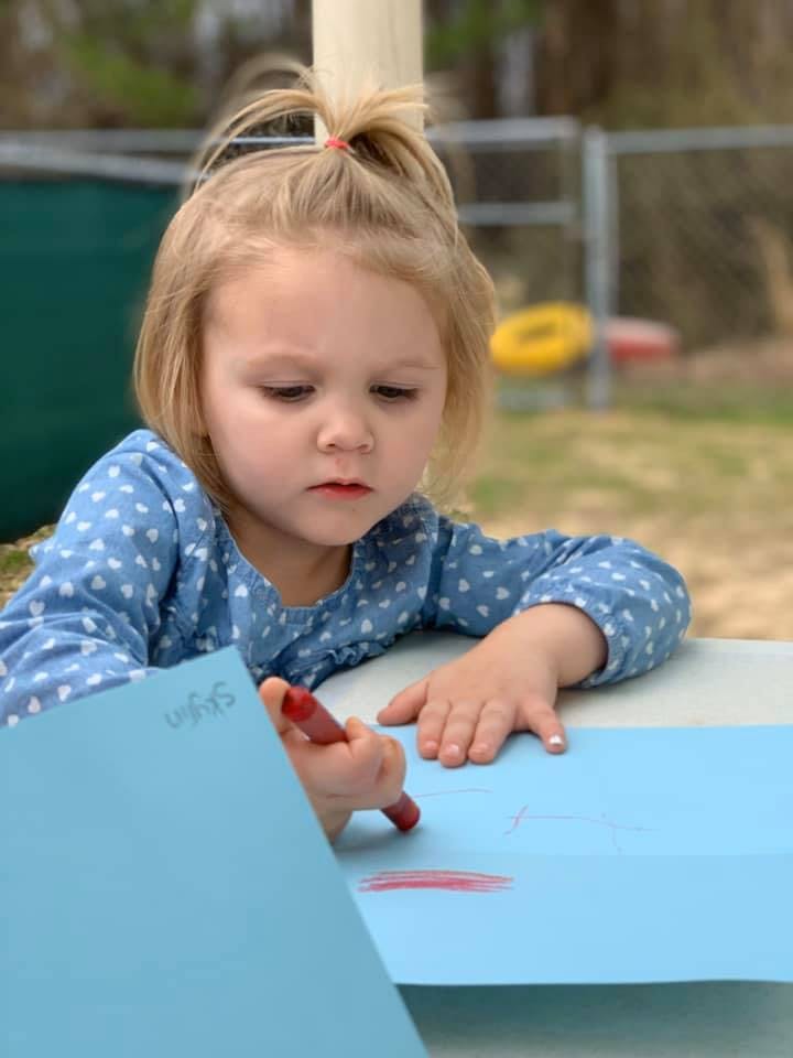 Child drawing on blue paper with a red crayon