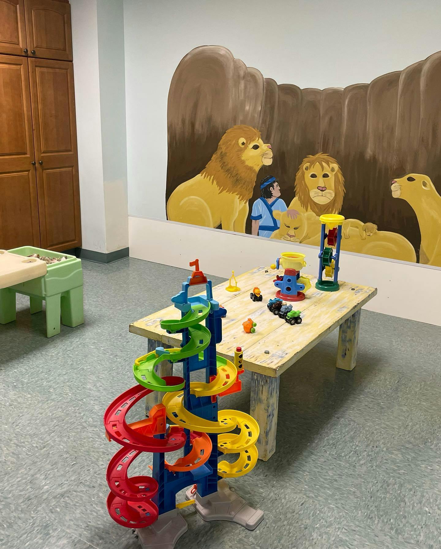 Toy car ramp and small table with toys in a room with a lion mural