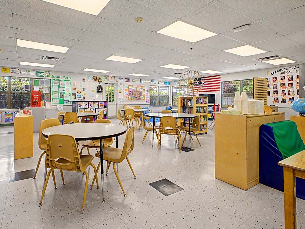 Empty classroom with small round tables and chairs, bookshelves, and an American flag