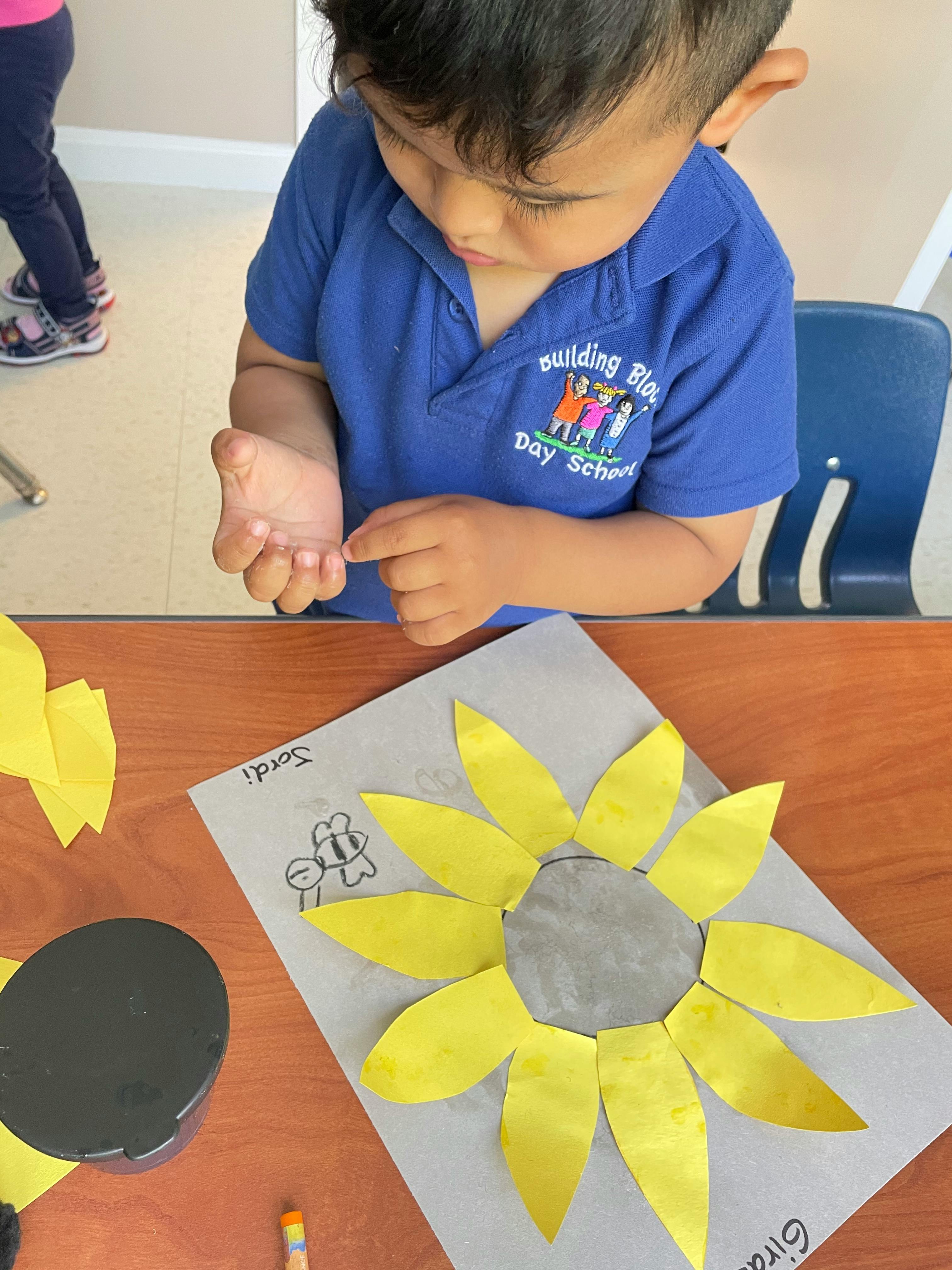 Child looking at their hand while sitting at a table with a paper sunflower craft