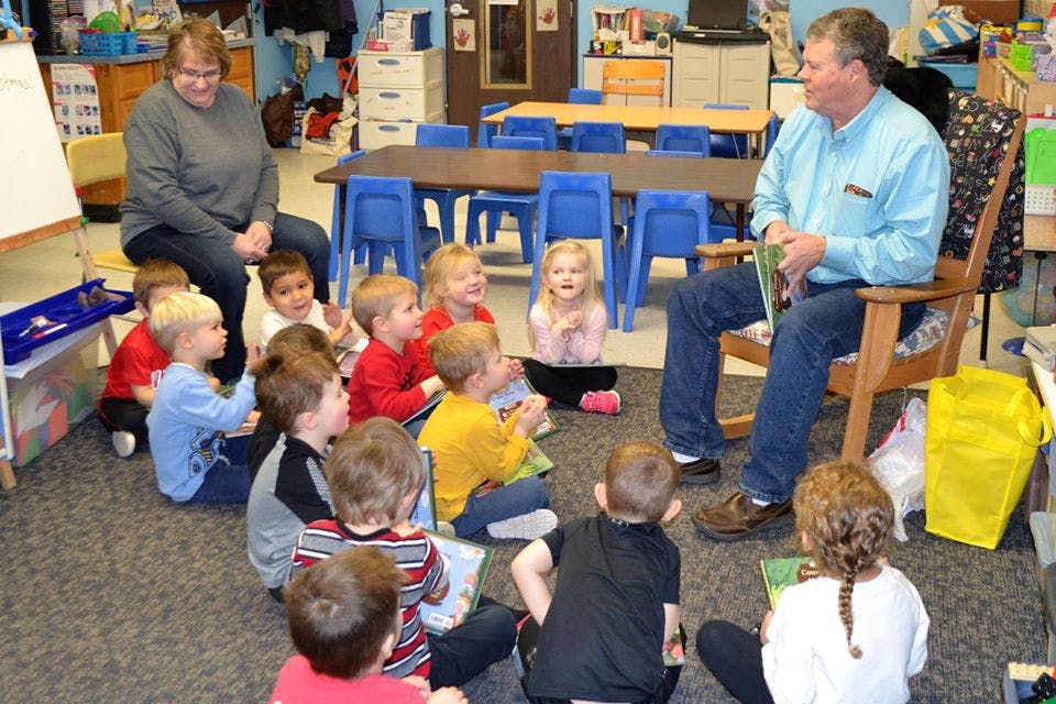 Adults reading to children sitting on the floor in a classroom