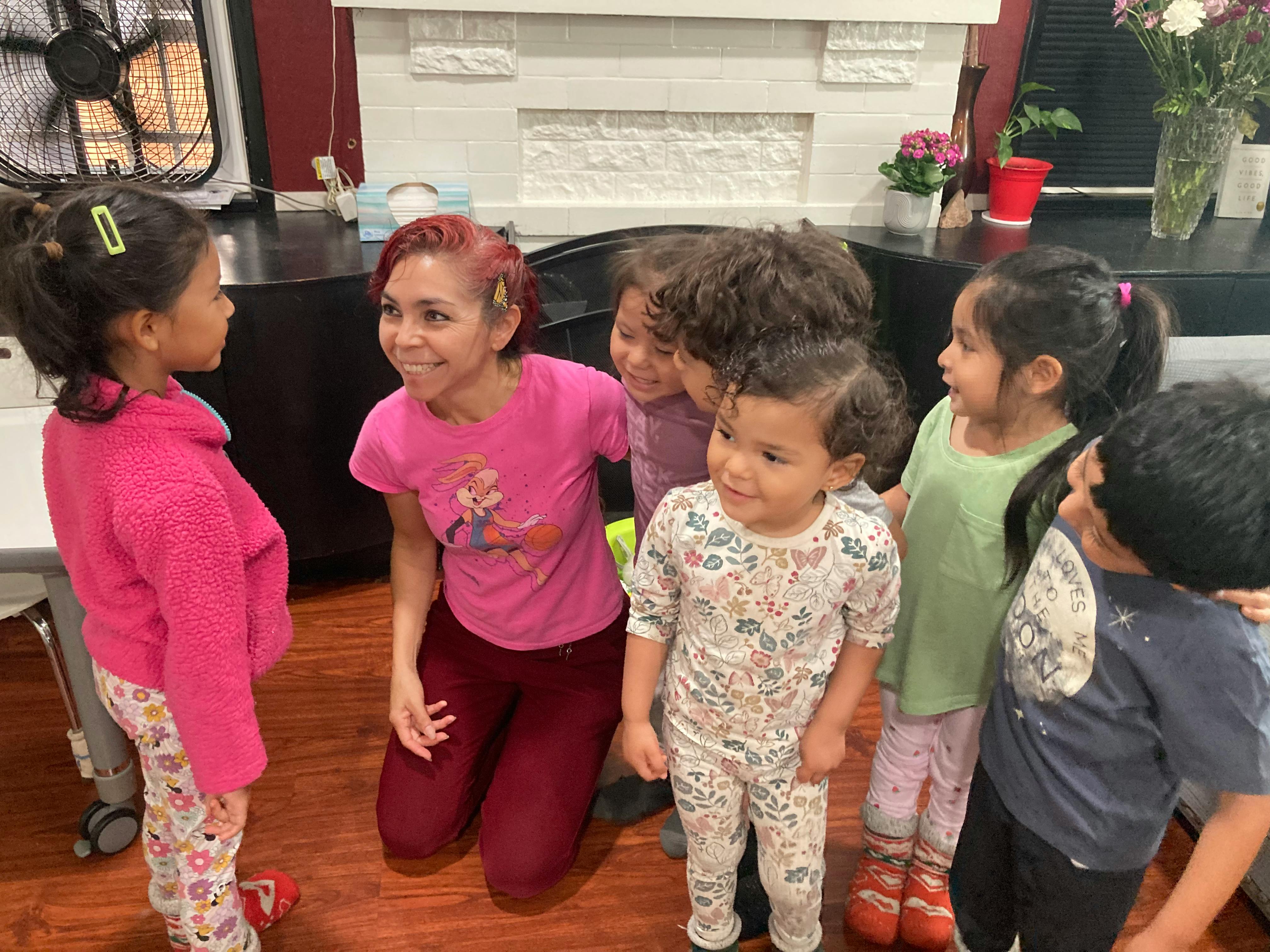 A person kneeling on the floor surrounded by a group of children