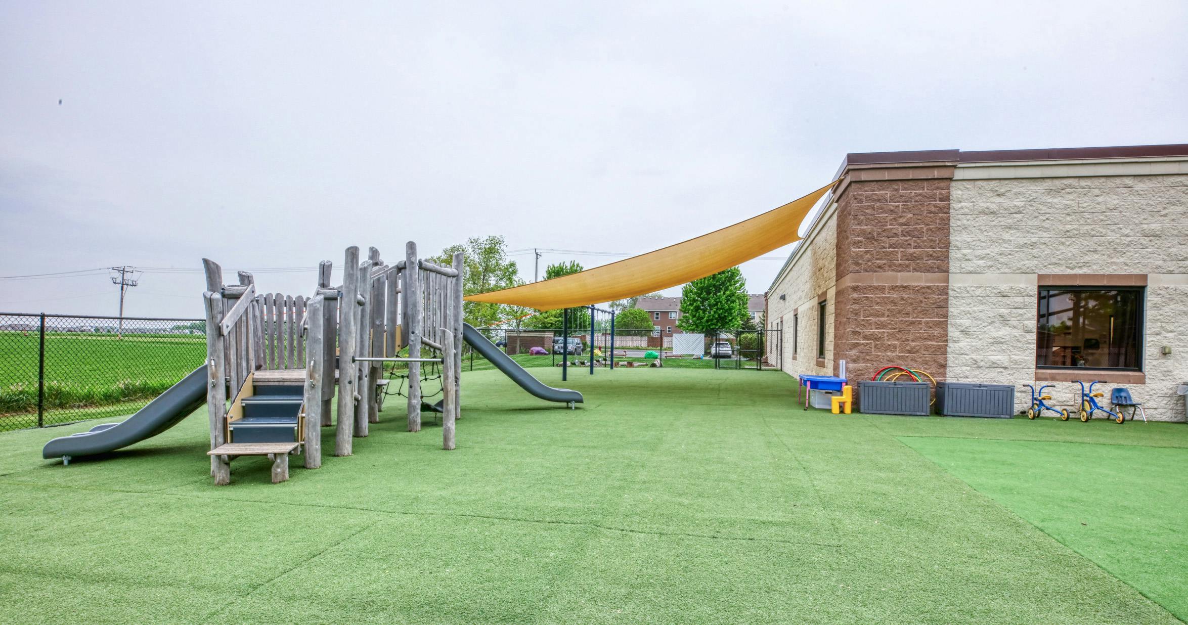 Playground with wooden climbing structure and slide on a green turf field