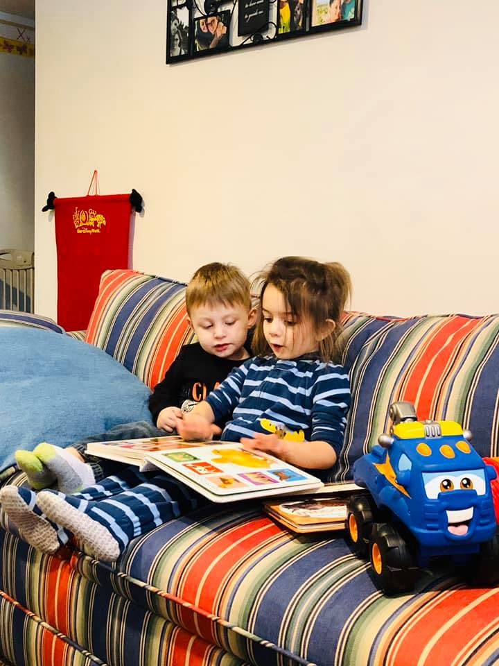 Two children sitting on a couch reading a book together
