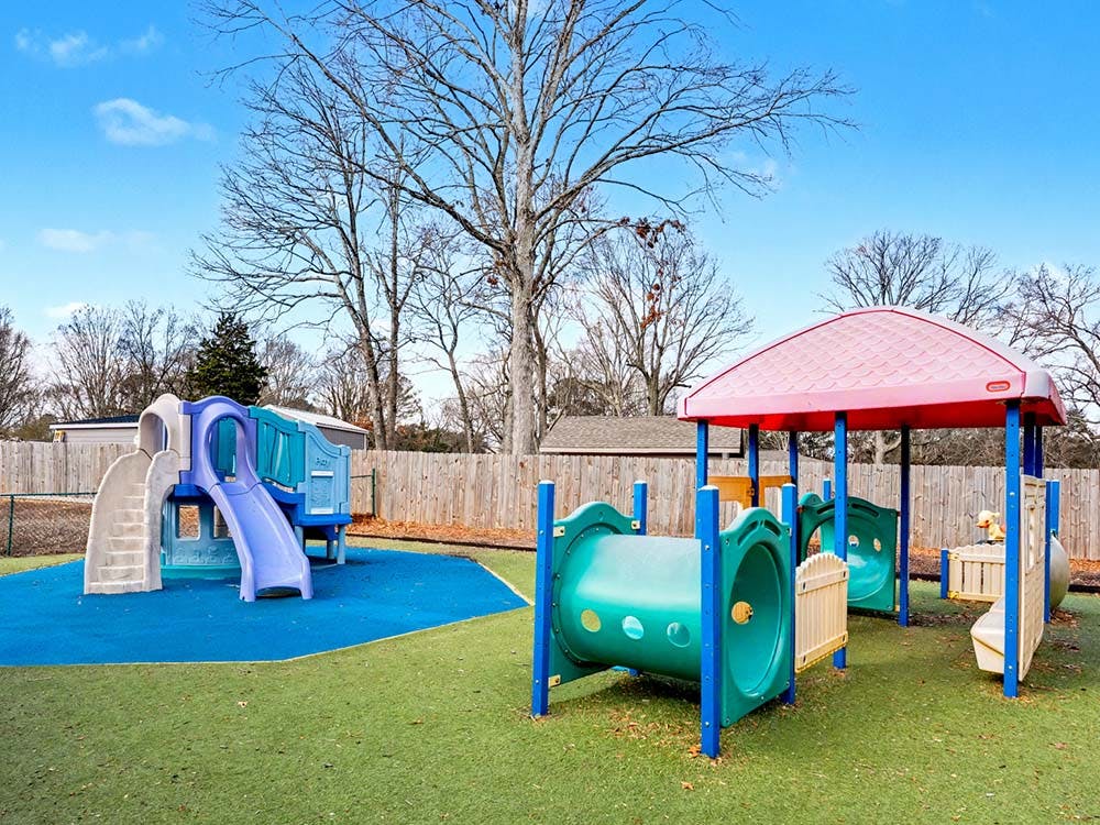 Colorful playground equipment on artificial turf with trees in the background