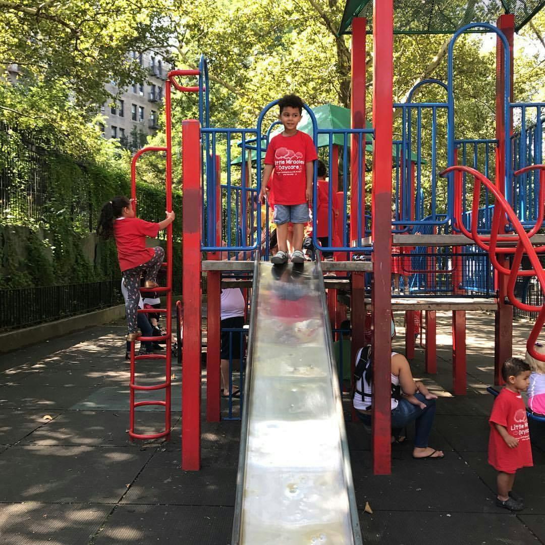 Child standing on a slide, another child climbing a ladder on playground structure in a playground