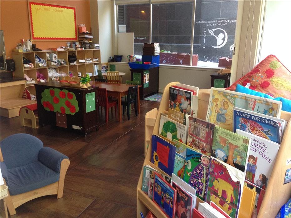 Children's classroom with book display, small tables and chairs, and a whiteboard with "FALL INTO SCHOOL"