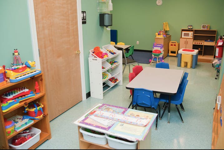 Classroom with small tables and chairs, shelves with toys