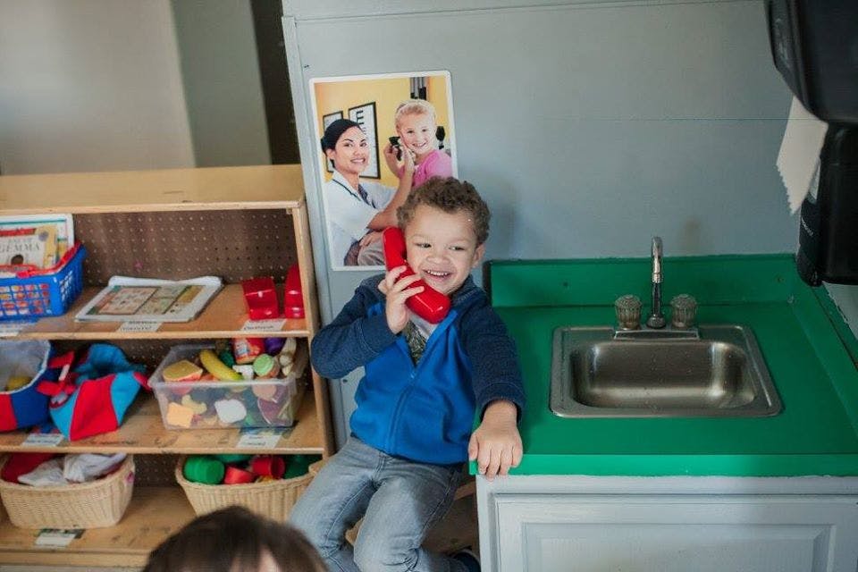Child holding a red toy phone to their ear in a play kitchen
