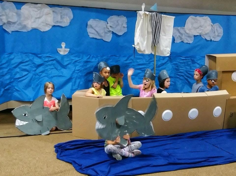 Children in a play with cardboard boat and shark props