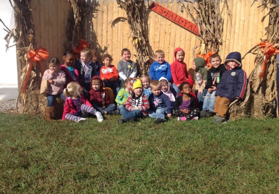 Group of children sitting on grass in front of corn stalks
