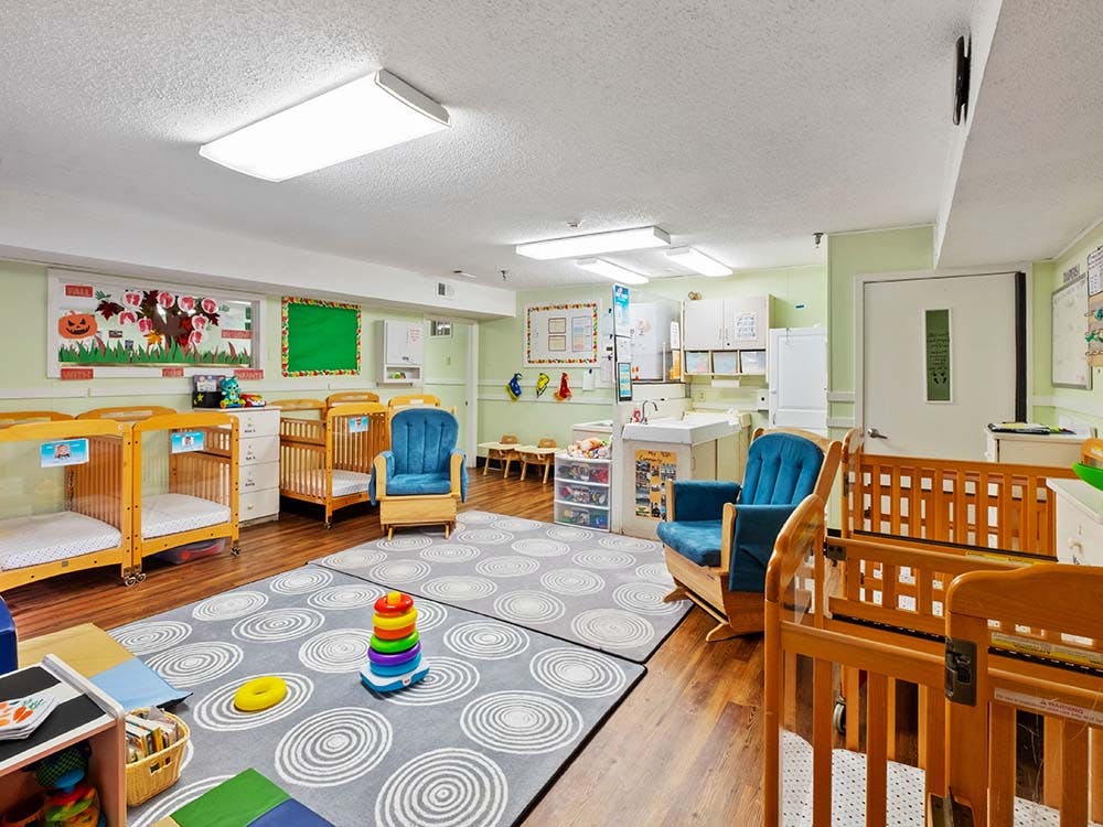 Cribs, rocking chairs, and play area in a daycare room