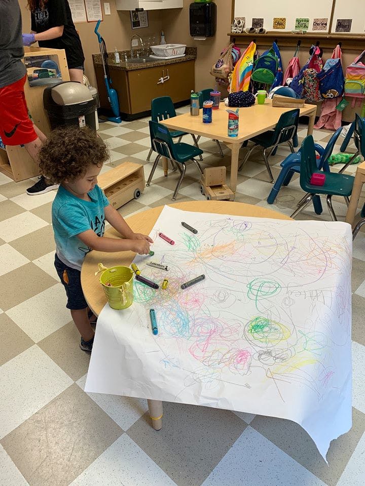 Child drawing on large paper with crayons in a classroom