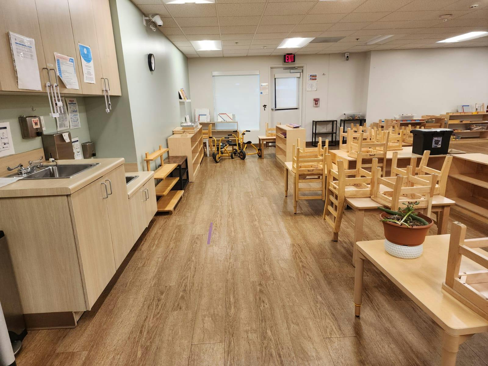 Classroom with child-sized tables and chairs, a sink, and storage cabinets