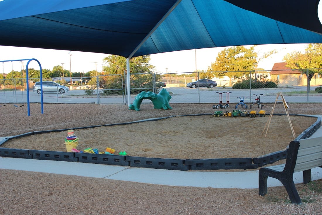 Playground with sand, swings, and a small climbing structure under a shade