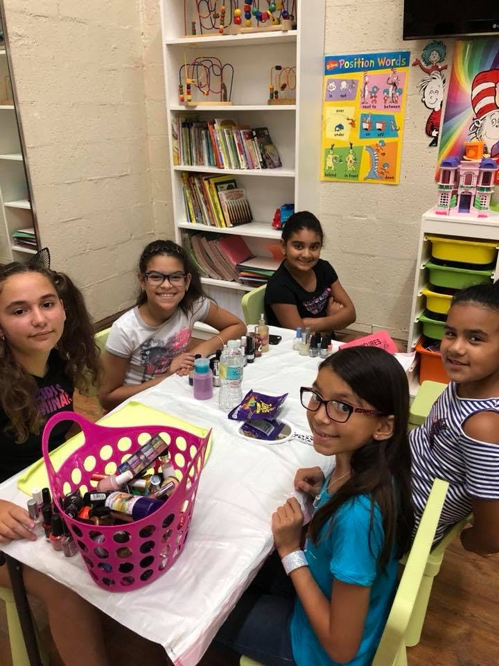 Four children sitting at a table with a basket of nail polish