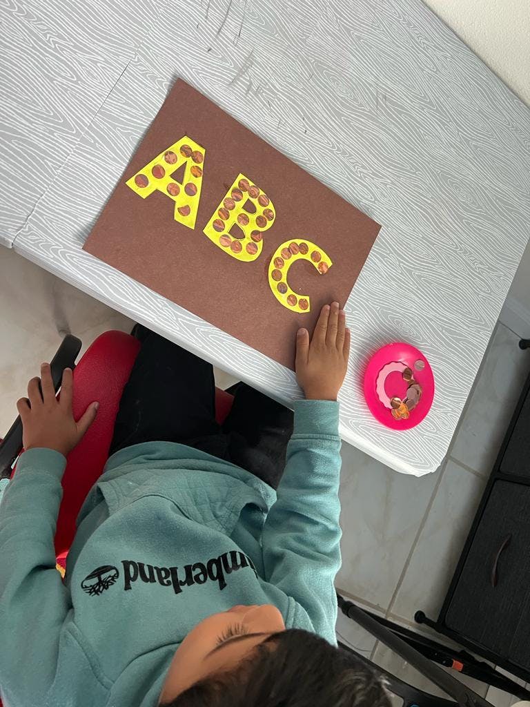Child sitting at a table with a craft project displaying "ABC"