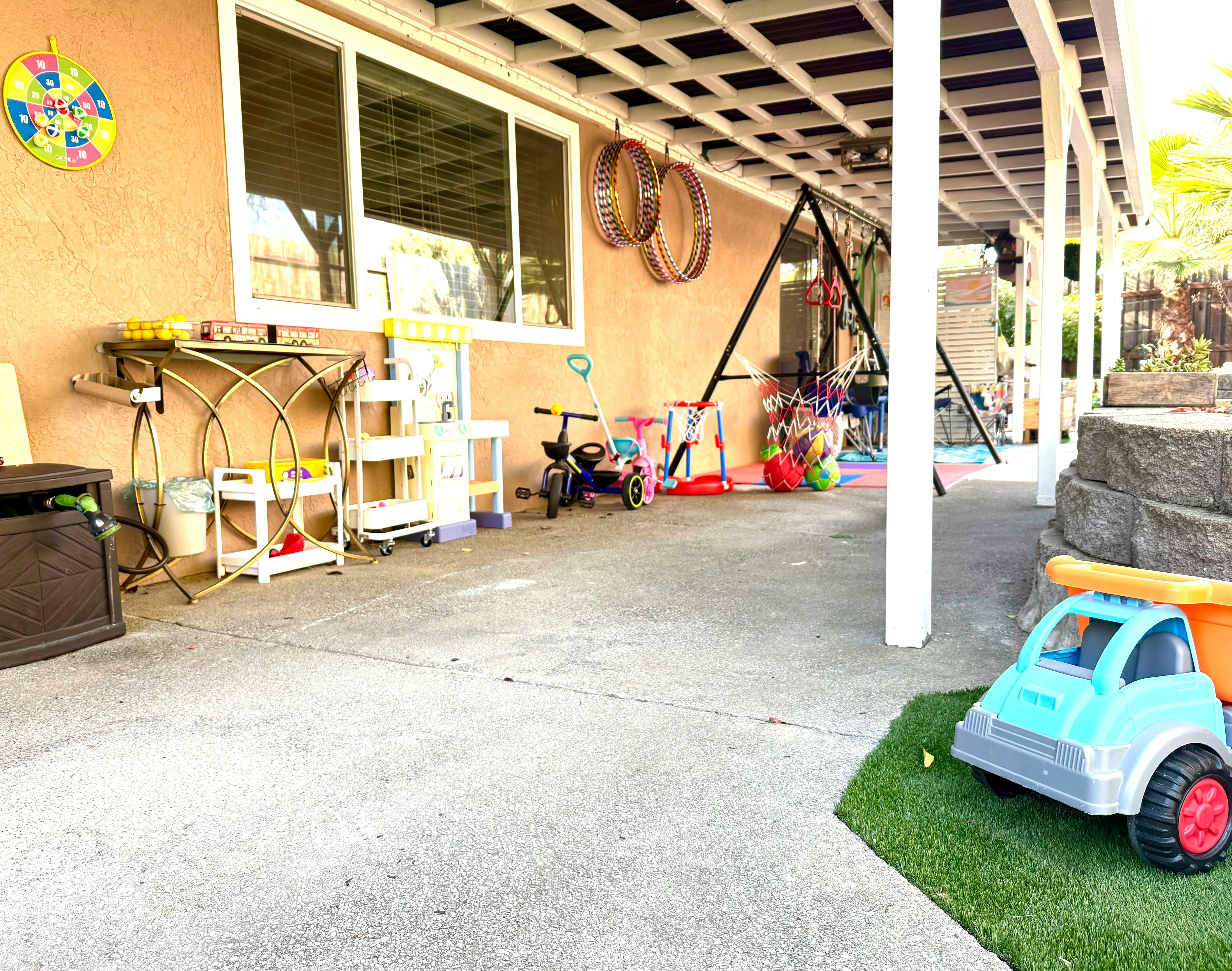 Patio with children's toys, including a tricycle, swing set, and toy truck