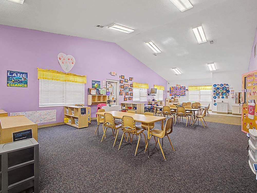 An empty classroom with tables and chairs, decorated with student artwork