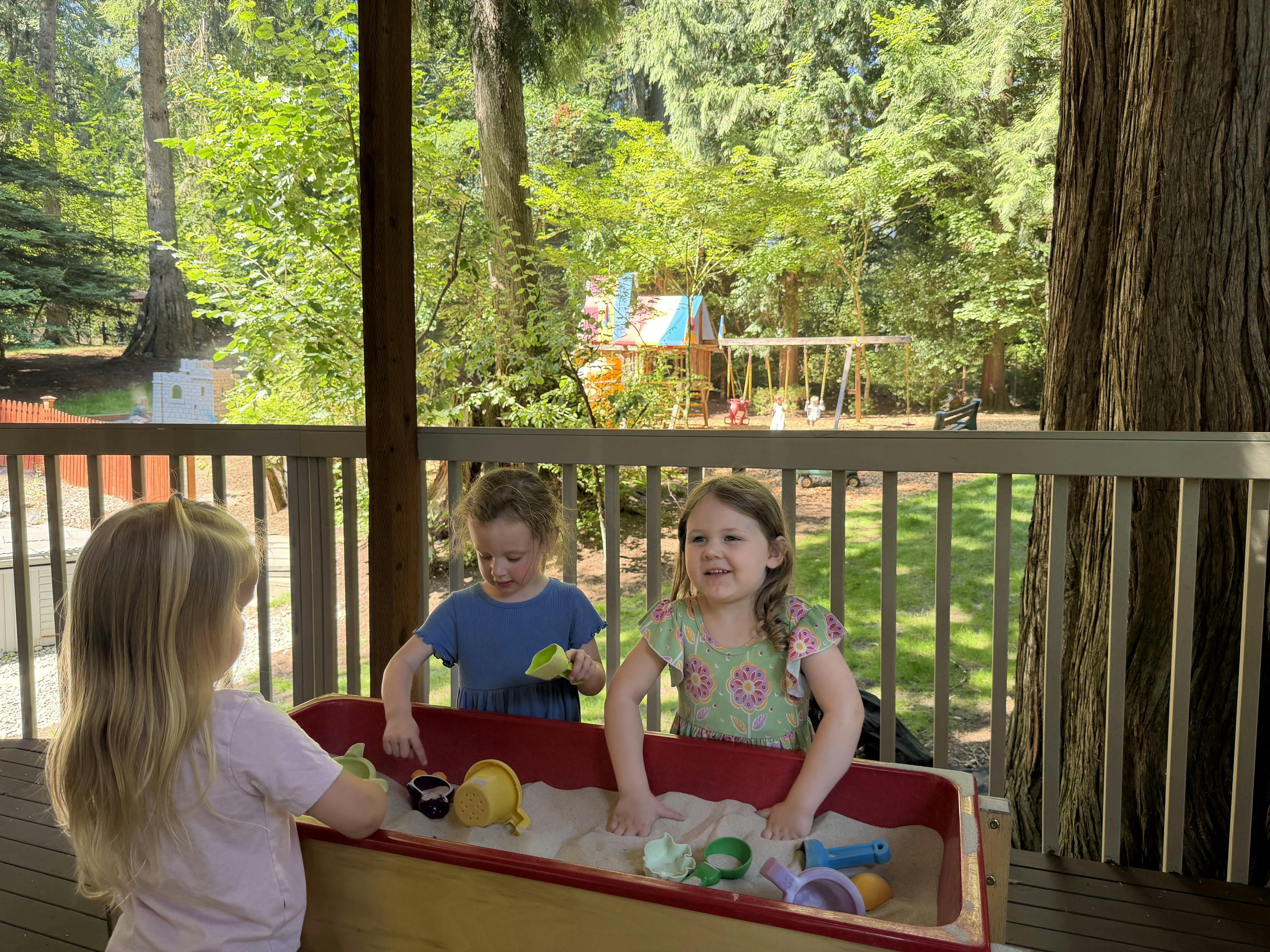 Three children playing with toys in a sandbox on a deck