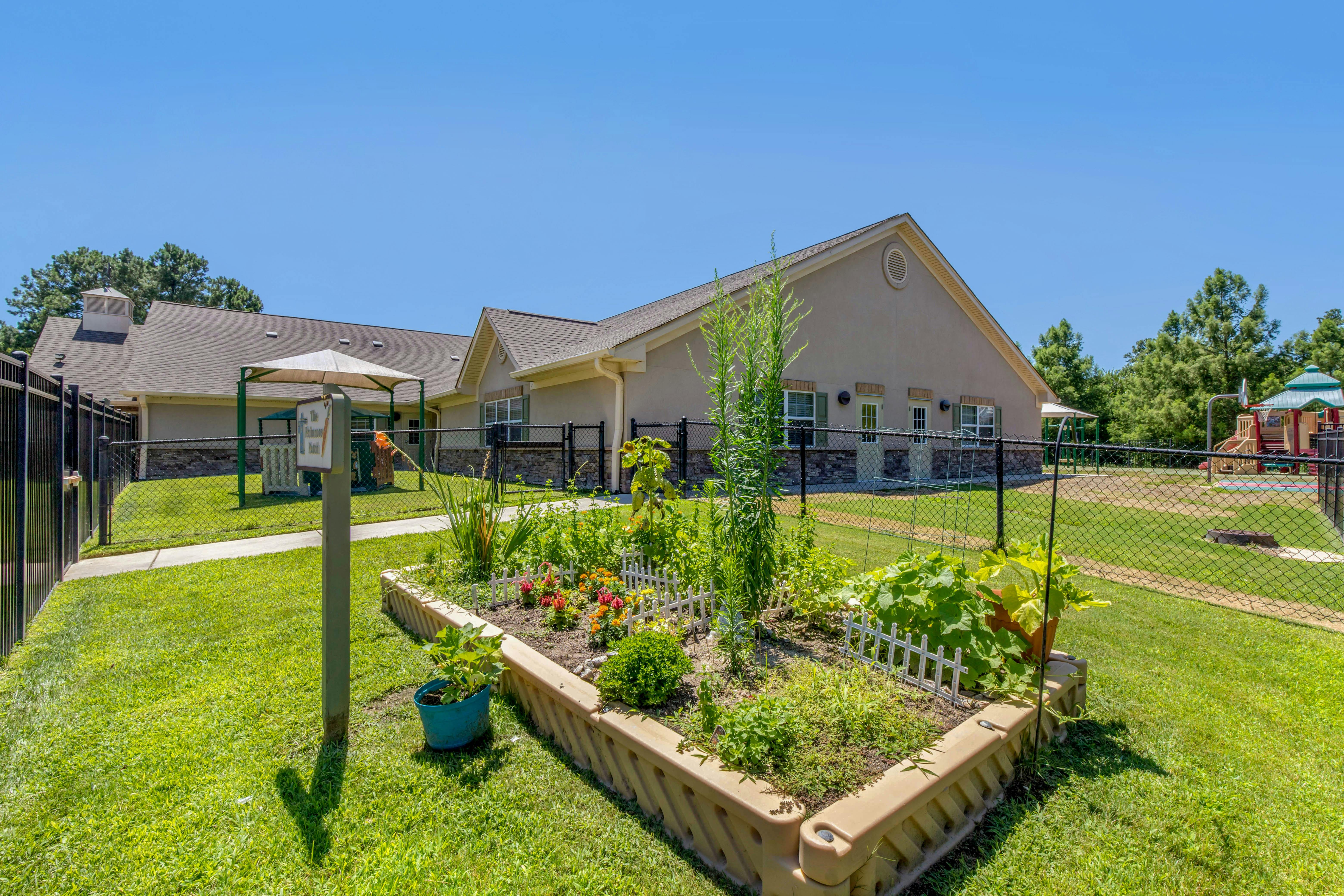 Raised garden bed in a grassy fenced area with a building in the background