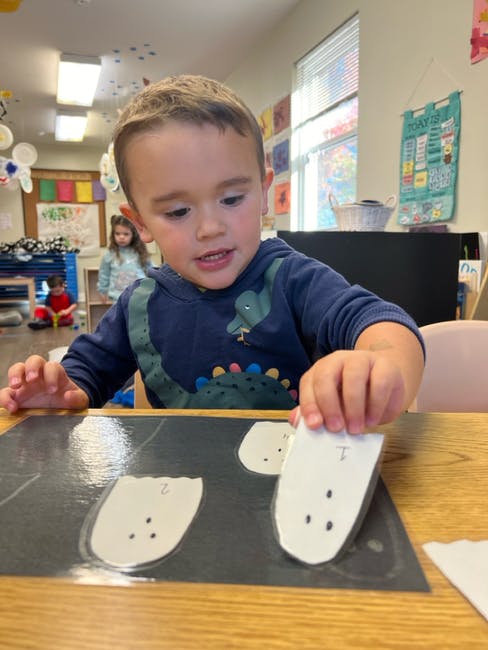 Child placing paper ghosts on a black mat in a classroom