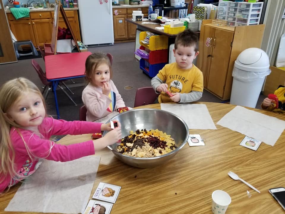 Three children mixing ingredients in a large bowl at a table