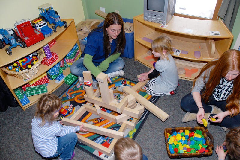 Adult and children playing with wooden blocks on a rug