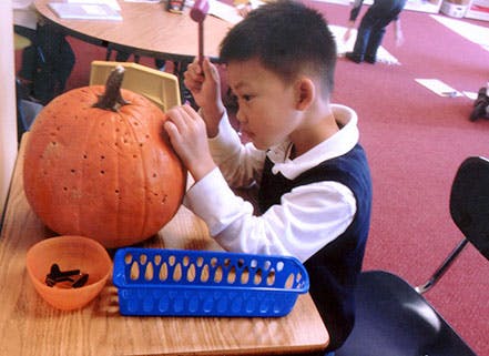Child using a mallet to poke holes in a pumpkin
