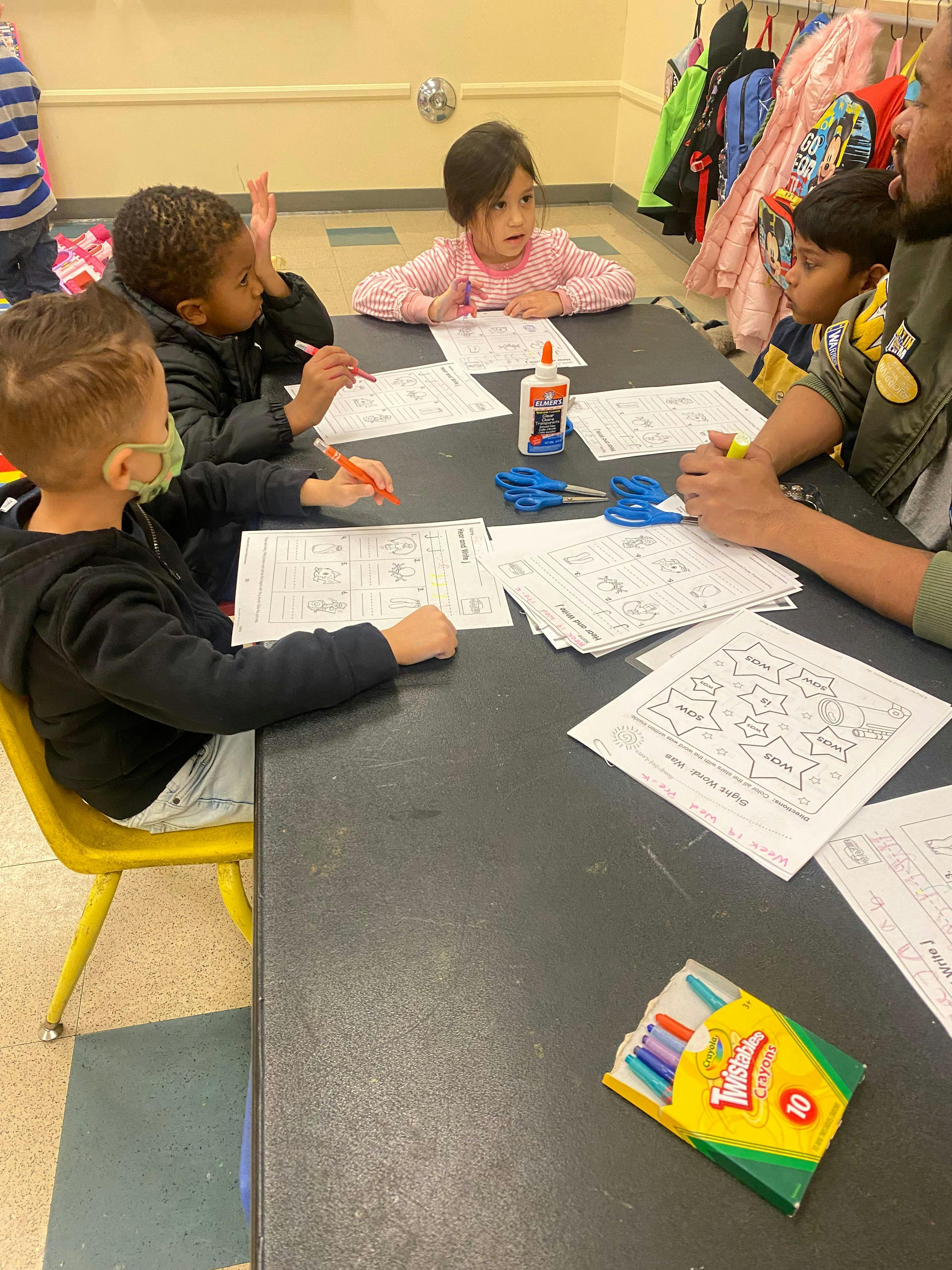 Children and an adult at a table with papers, glue, and scissors