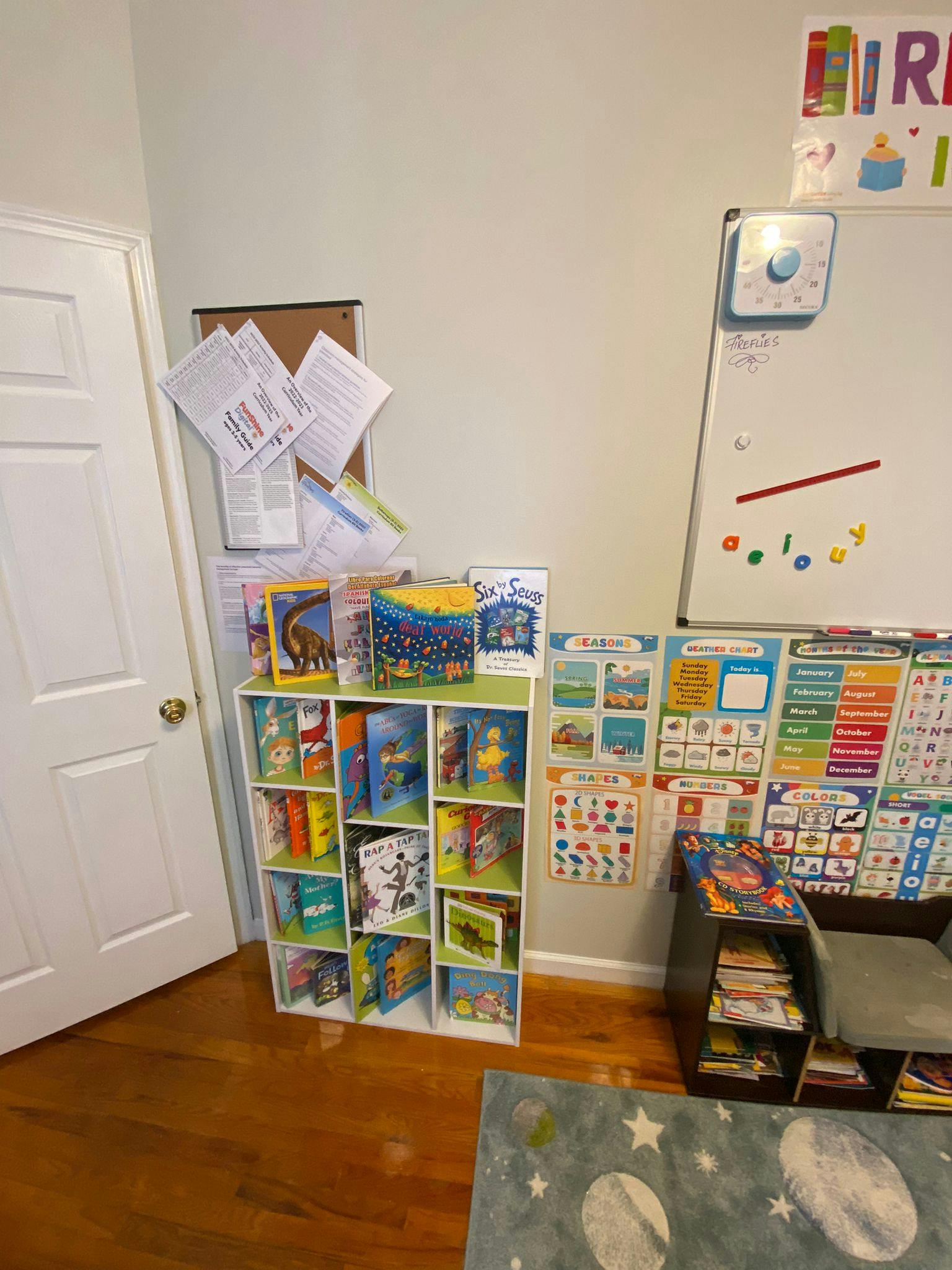 Bookshelf with children's books next to a whiteboard and educational posters