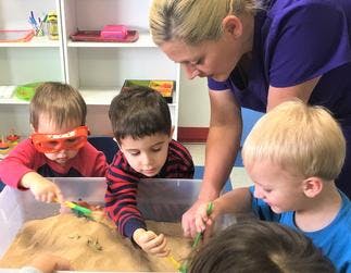 Adult and three children playing in a sand table