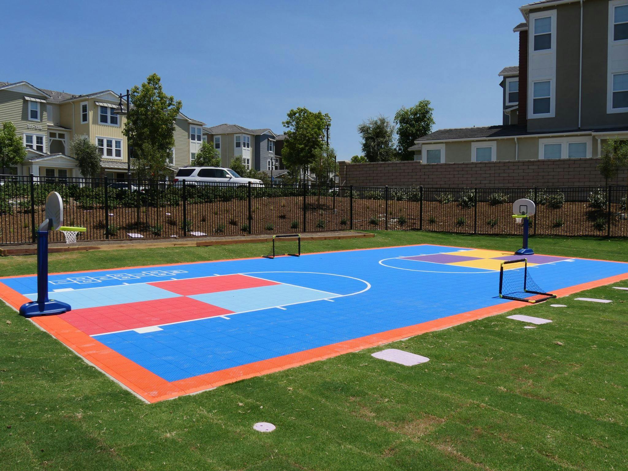 Outdoor basketball court with blue, red, and yellow sections on green grass