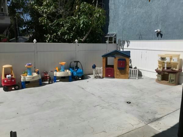 Outdoor play area with various toys including a playhouse and ride-on cars