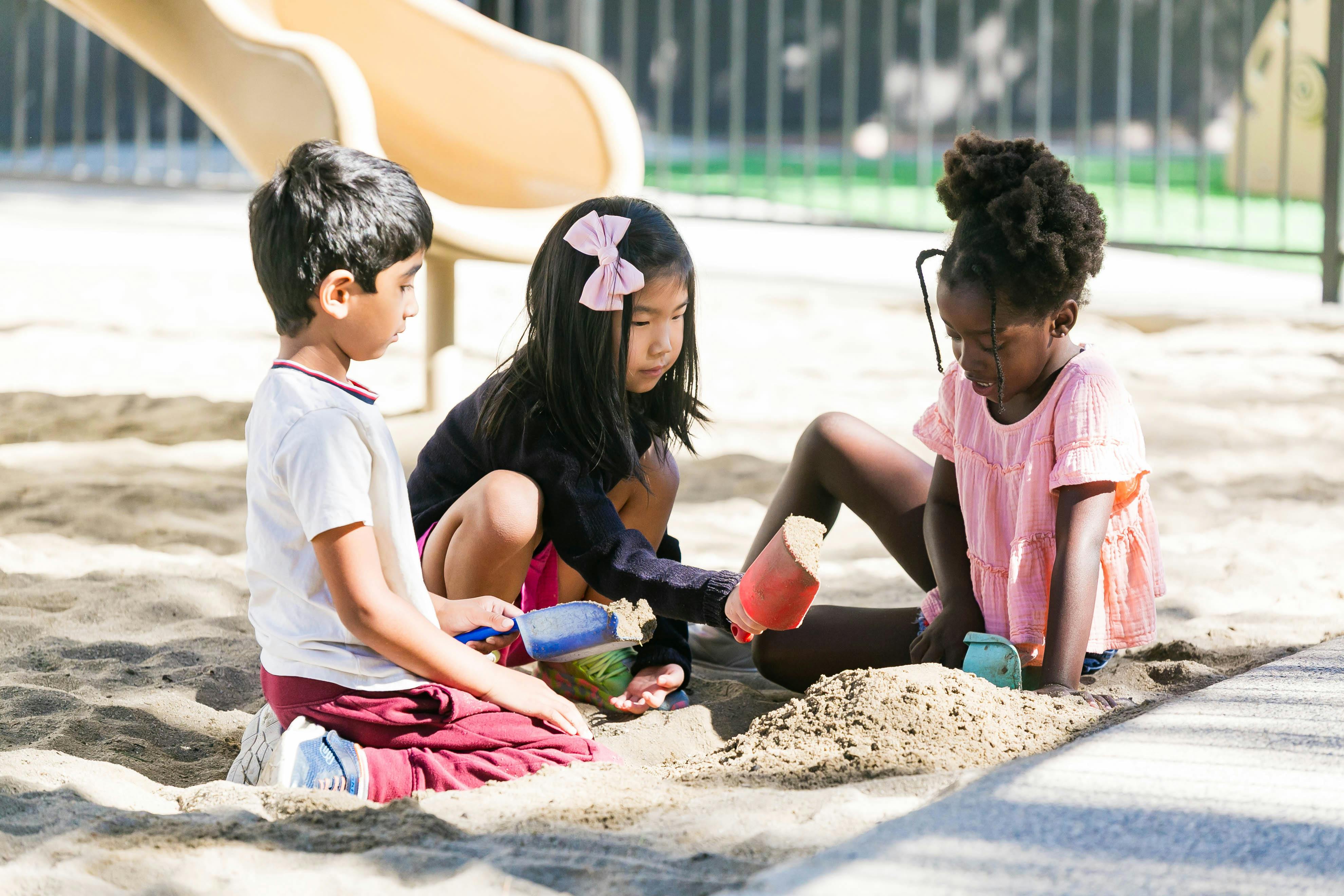 Three children playing in a sandbox with sand toys