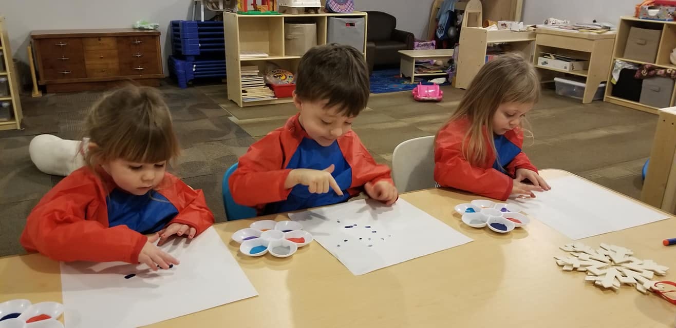 Three children painting at a table in a classroom
