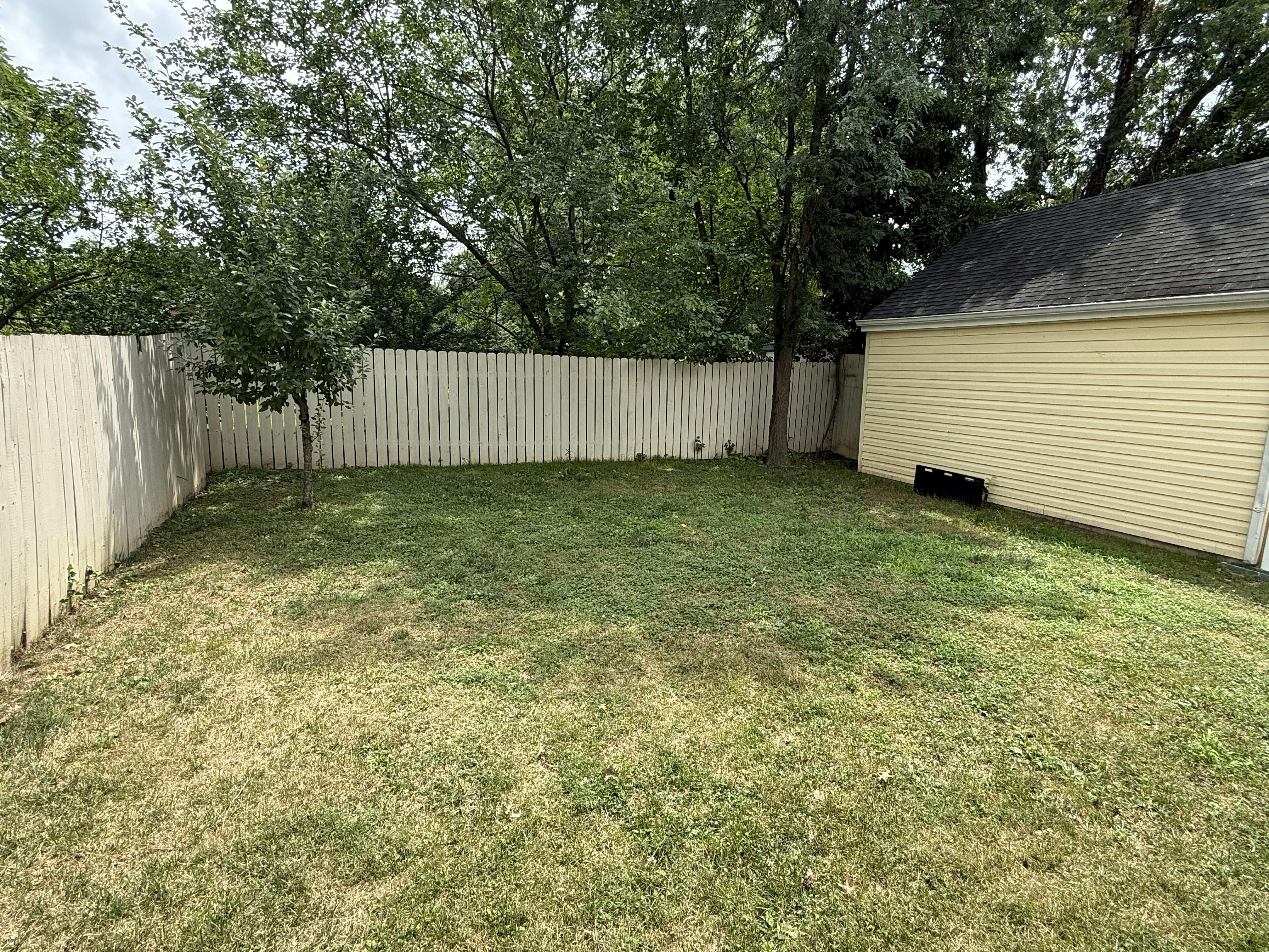 A grassy backyard with a white fence and a yellow garage