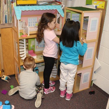 Three children playing with a dollhouse