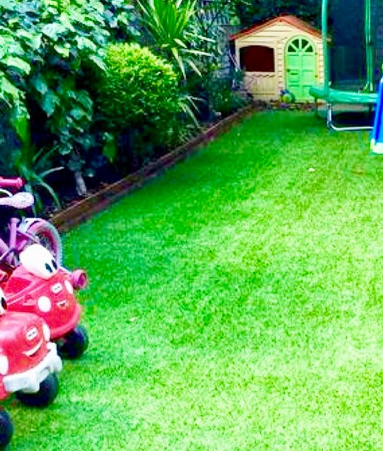 Red toy cars on artificial grass with a playhouse in the background