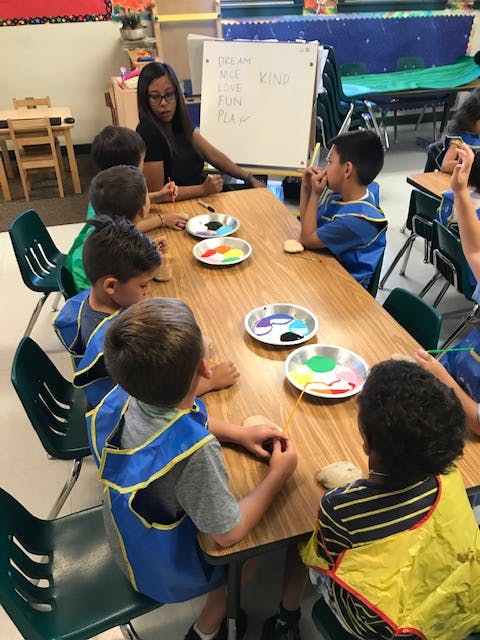 Adult and children at a table with paint palettes in a classroom