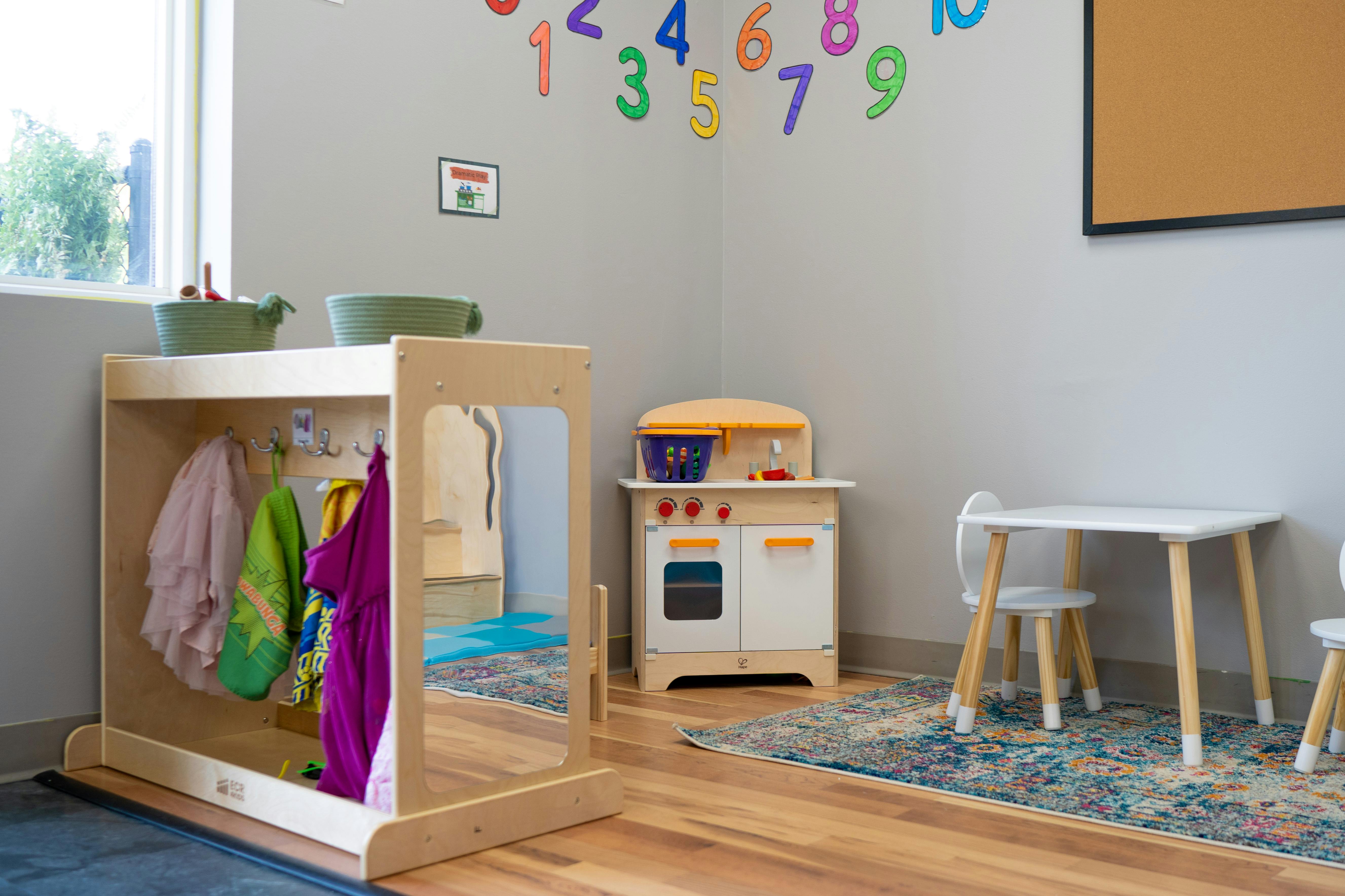 Children's play area with a small kitchen, table, and clothes rack