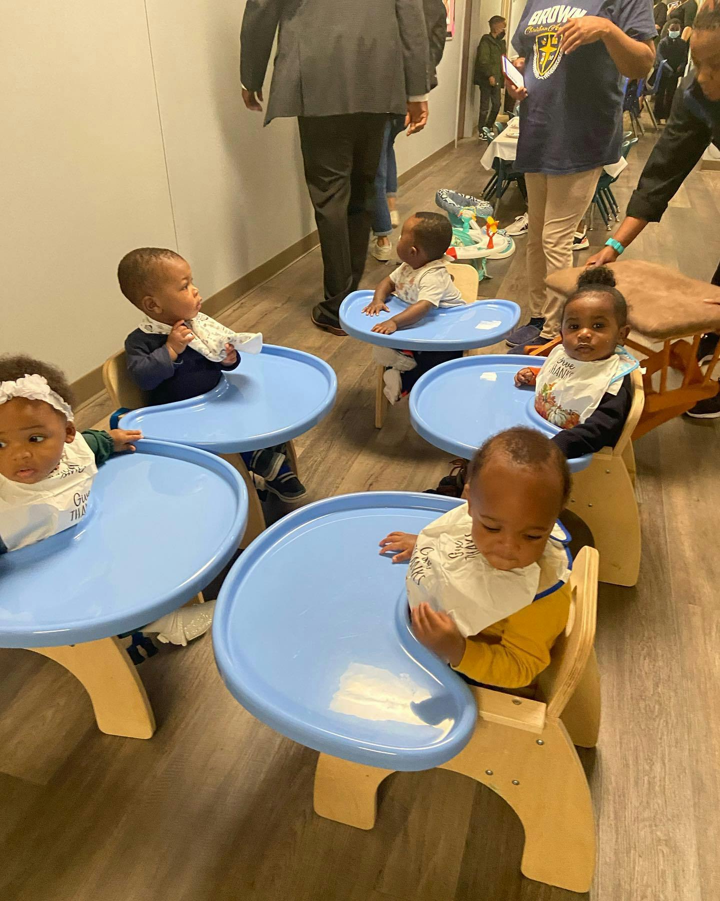 Multiple babies sitting in high chairs with blue trays