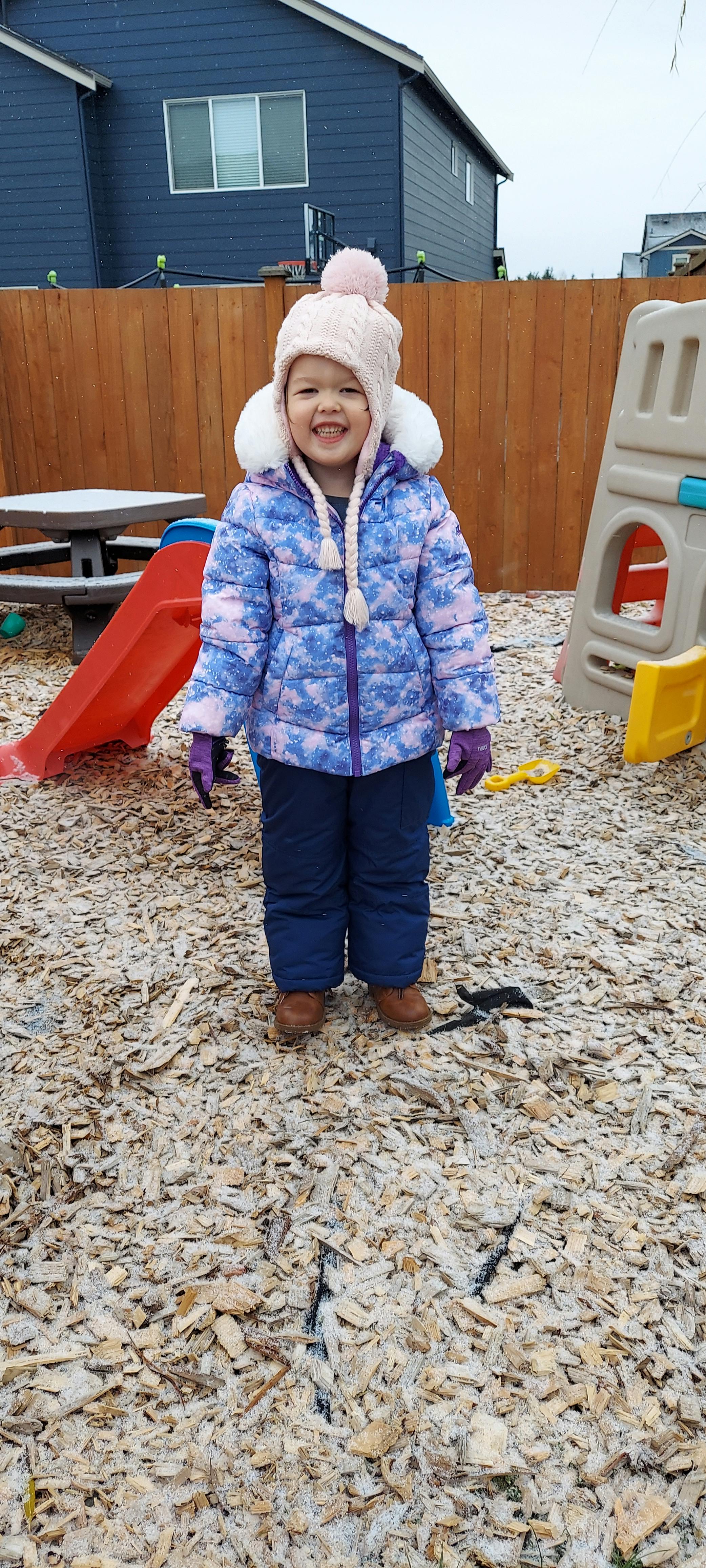 Child in winter coat and hat standing on wood chips in a playground