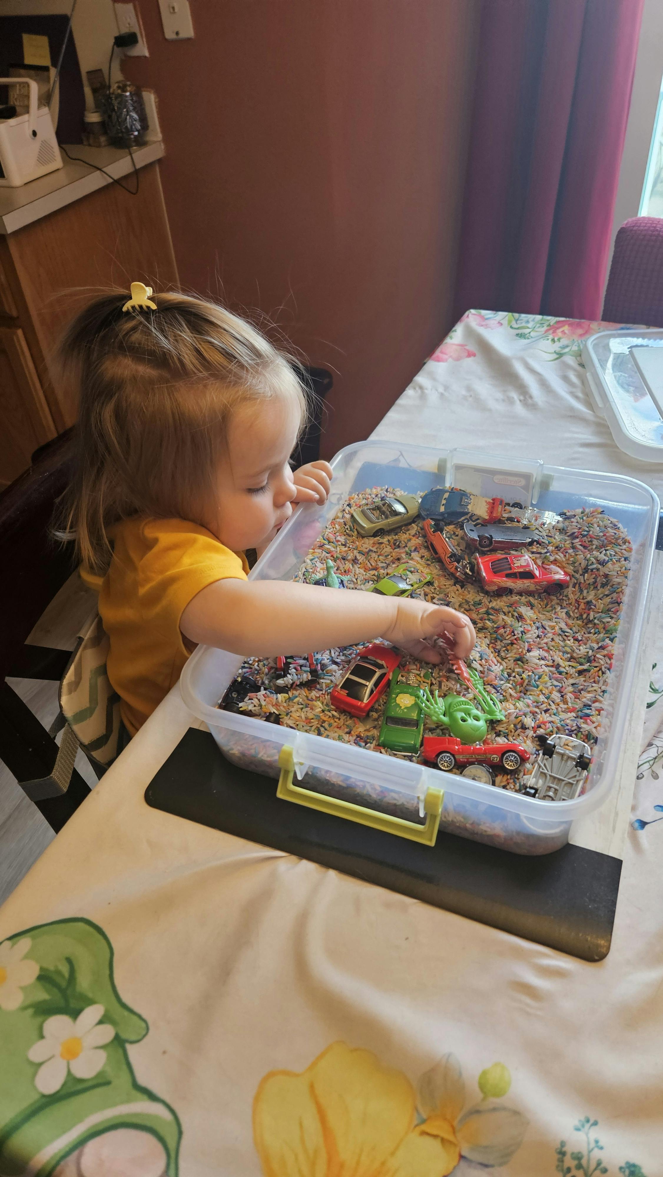 Child playing with toy cars in a sensory bin