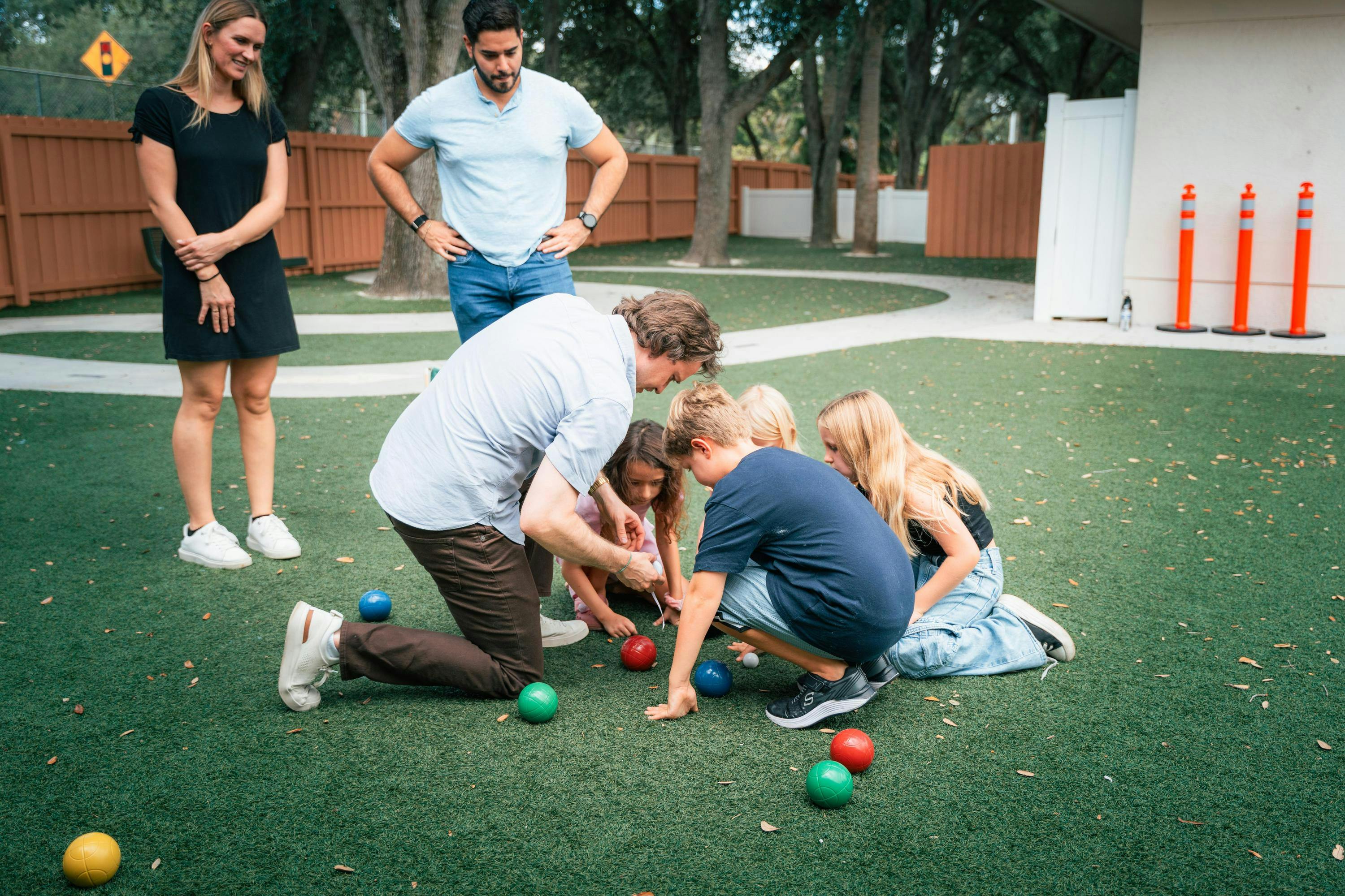 Adults and children playing with bocce balls on artificial grass